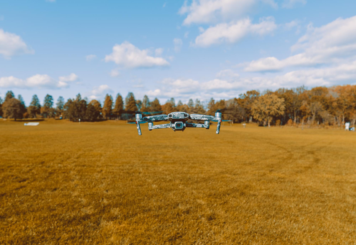 Un dron azul y blanco vuela sobre un campo dorado bajo un cielo claro.