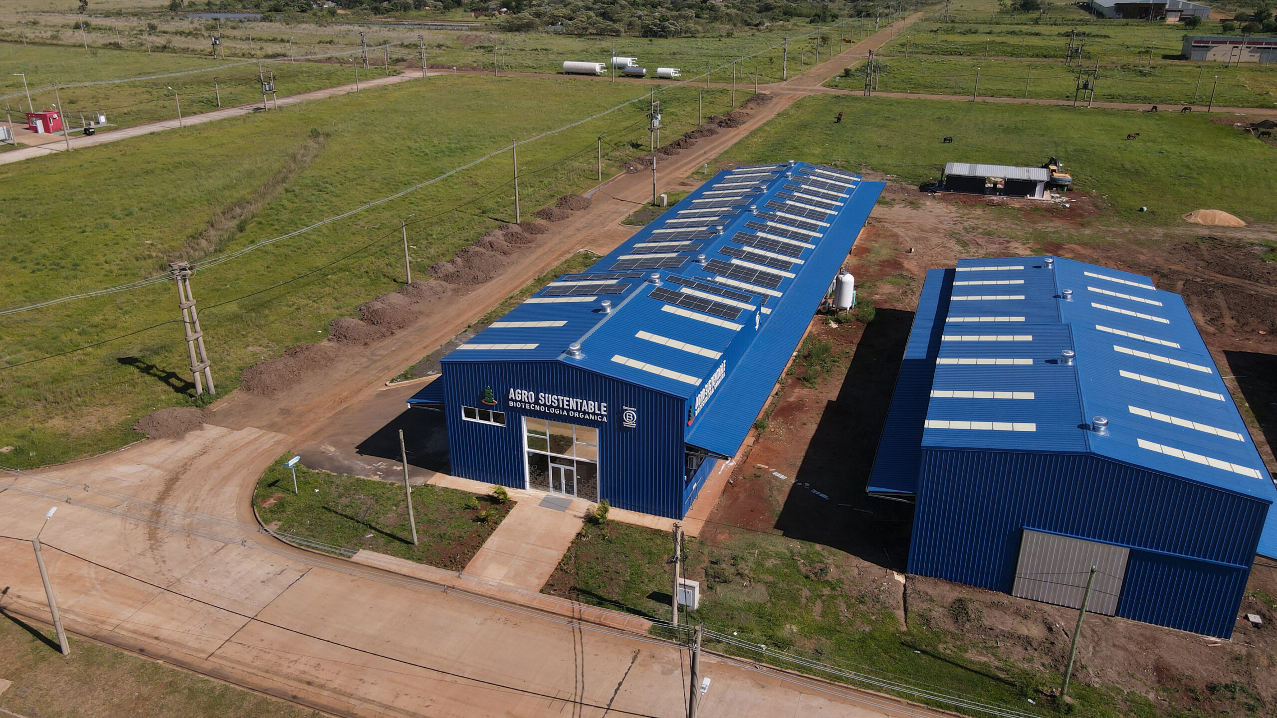 Vista aérea de las instalaciones de Agro Sustentable, con techos azules equipados con paneles solares en un entorno verde y tecnológico.