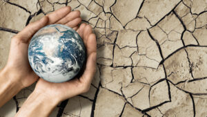 Manos humanas sostienen el planeta Tierra sobre un fondo de suelo seco y agrietado, simbolizando la urgencia climática y la necesidad de proteger los recursos naturales.