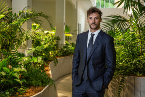 Hombre con traje oscuro posando junto a plantas en un entorno interior con luz natural
