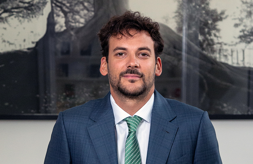Joaquín Basanta con traje azul y corbata verde posando en interior institucional.