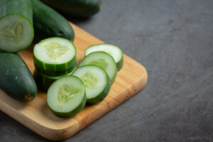 Rodajas de pepino fresco sobre una tabla de madera, listas para consumo, representando producción hortícola sustentable.