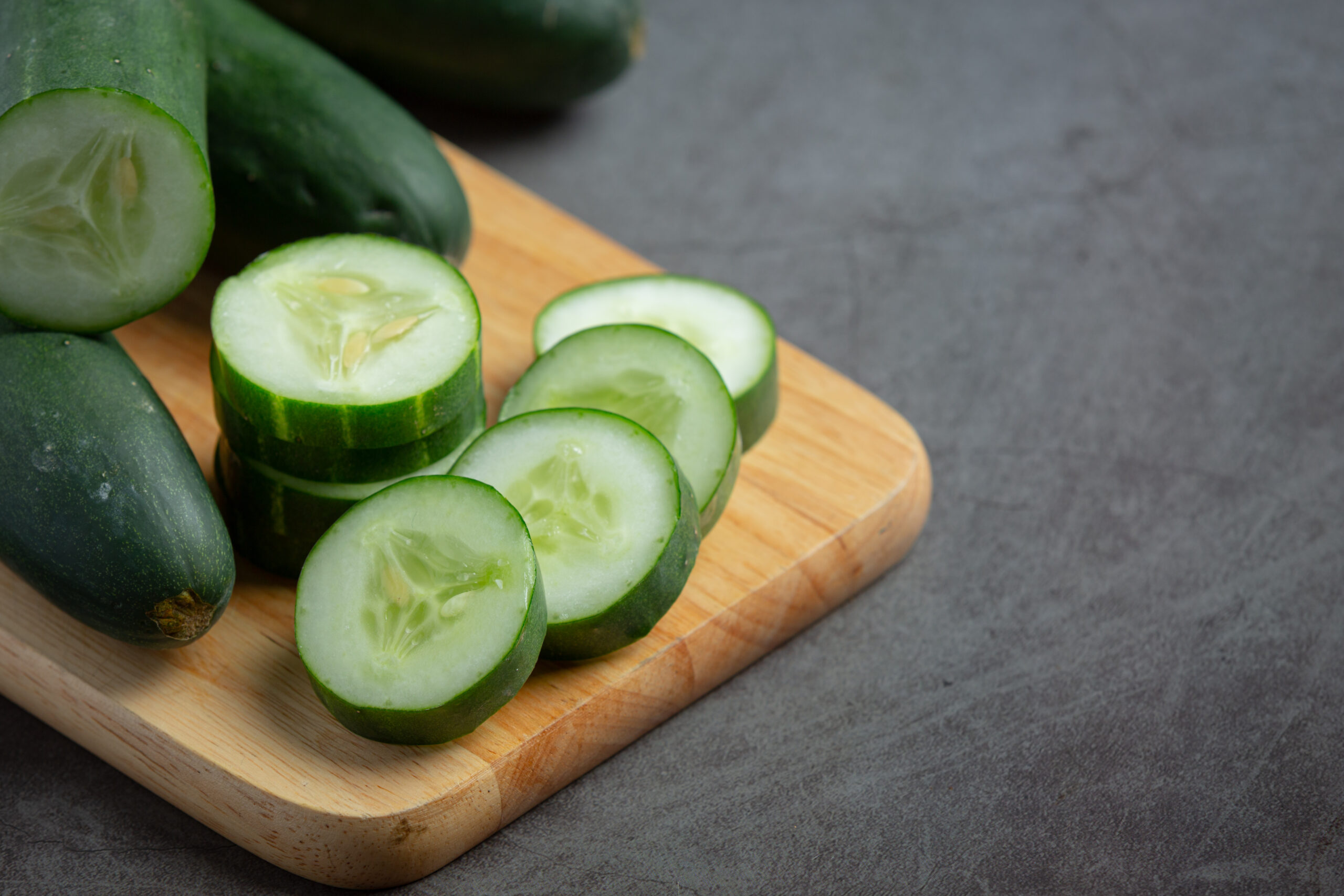 Rodajas de pepino fresco sobre una tabla de madera, listas para consumo, representando producción hortícola sustentable.